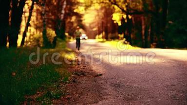 运动男在柏油路跑步。 乡村城市公园。 绿树森林和地平线上的阳光。
